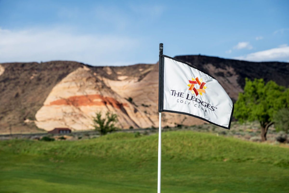 White flag on a golf course pole featuring The Lodge Golf Club logo, with rocky hills and blue sky in the background.